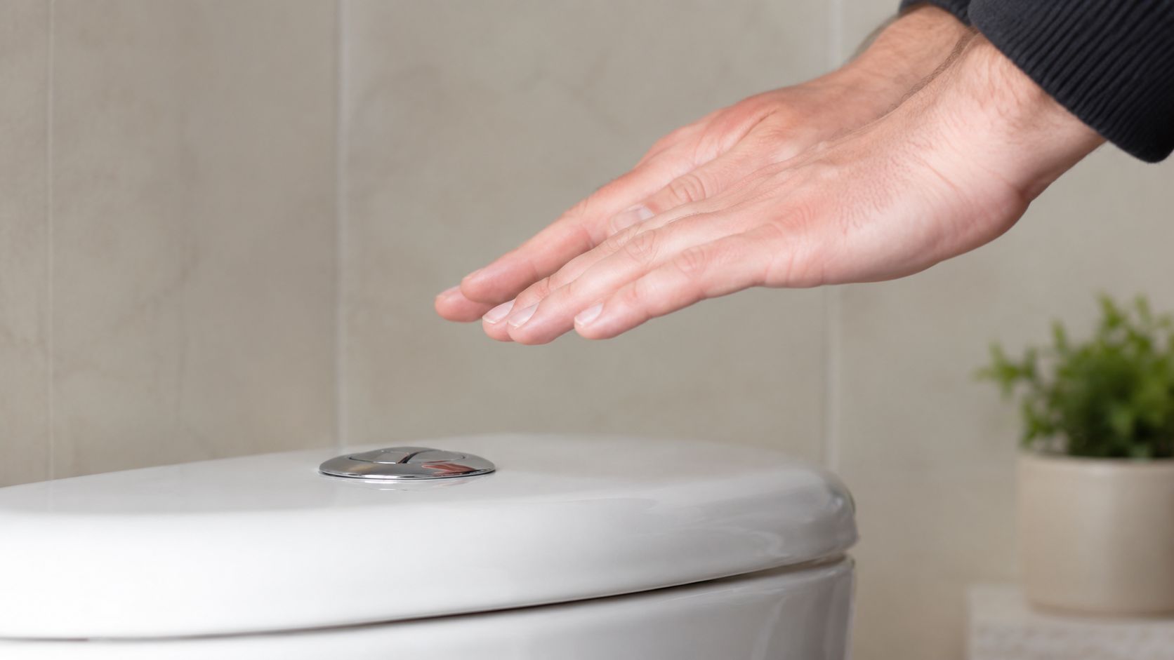 En person aktiverer et berøringsfrit toilet med hånden for en hygiejnisk og effektiv skylning på badeværelset.